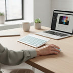 digitaley.co pastel blue wireless keyboard and mouse set on a wooden desk with a laptop and coffee cup.